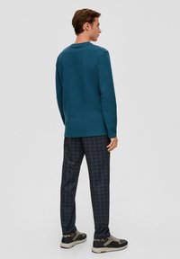 Teal langemouwshirt met een ronde hals, gecombineerd met donkere geruite broeken en grijs-zwarte sneakers. Glad textuur, ontspannen pasvorm.