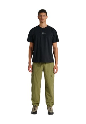 Czarna bawełniana koszulka z logo z przodu, w połączeniu z oliwkowozielonymi spodniami cargo z wieloma kieszeniami, noszona z brązowymi butami trekkingowymi.