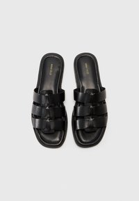 Black slide sandals made of smooth leather, featuring a woven strap design and a flat sole with a square toe. No visible hardware.