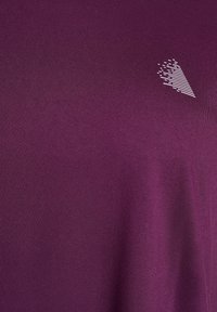 Lila Kurzarmhemd aus glattem Stoff; mit einem kleinen weißen geometrischen Logo auf der Brust; einfaches Design ohne Muster.