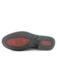 Suela de zapato de goma negra con un patrón elevado, que cuenta con un inserto acolchado rojo y un logo de marca en relieve. Texturizada para mayor agarre y estabilidad.