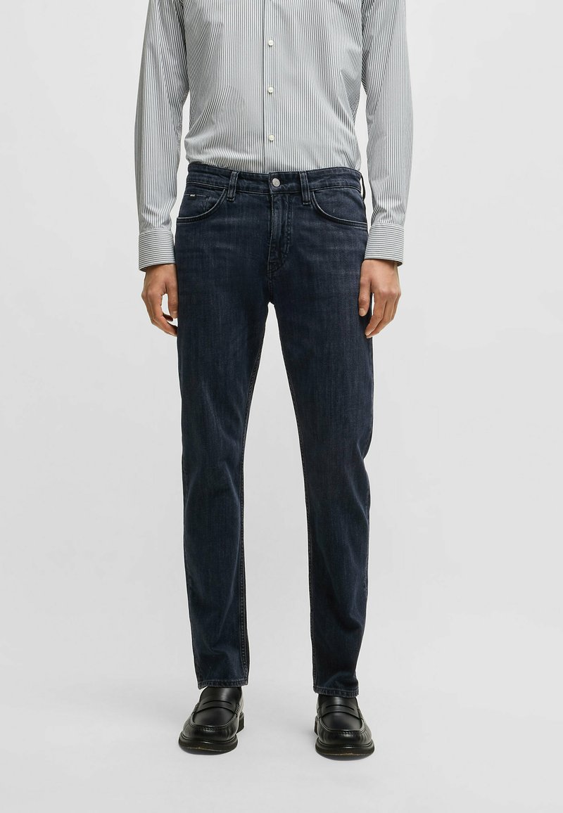 Mörkblå denimjeans med rak bendesign, femficksstil och subtila sömnadsdetaljer. Matchas med en randig skjorta med knäppning.