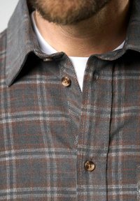 Camisa a cuadros grises con cuello abotonado, botones marrones y una textura suave. El patrón incluye detalles en blanco y naranja en el diseño a cuadros.