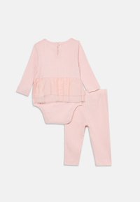Vaaleanpunainen ribbikuvioinen kaksiosainen asu, joka sisältää pitkähihisen paidan, jossa on tüllistä valmistettu peplum, yhteensopivat legginsit ja nappisuljenta takana.