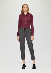 Chemise boutonnée à manches longues bordeaux associée à un pantalon gris texturé avec une taille élastique et un cordon de serrage, complété par des mocassins noirs.