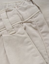 Beige bomullstyg med sömmar, knappstängning och vikbar midja, som visar en jämn, texturerad yta.