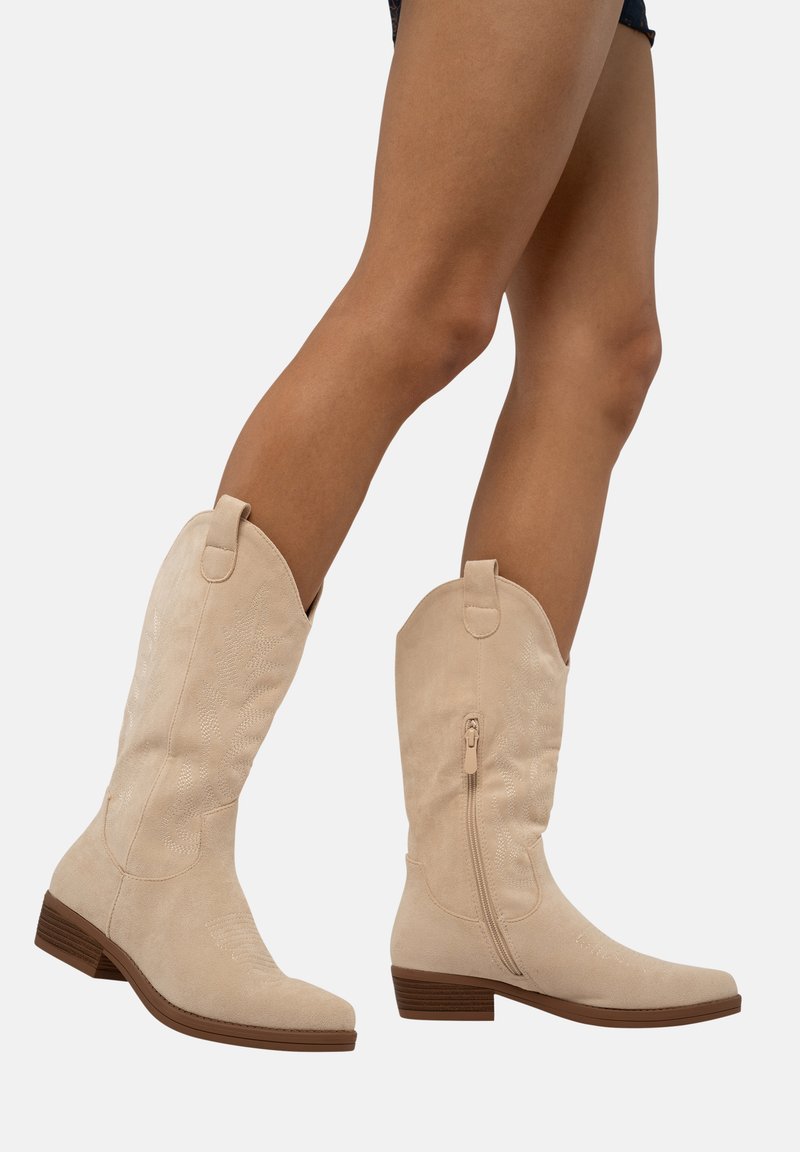 Botas de cowboy de ante beige con cremallera lateral, punta afilada y un patrón bordado en el caña. Tacón bajo apilado para mayor estabilidad.