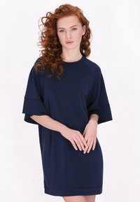 Granatowa, oversize sukienka T-shirt z krótkimi rękawami raglanowymi i okrągłym dekoltem, gładką teksturą oraz dołem, który sięga powyżej kolan.