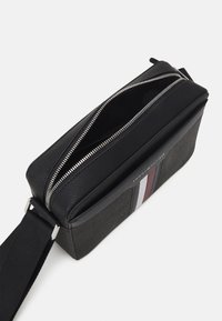 Borsa a tracolla nera in materiale sintetico con zip argentate, superficie testurizzata, una striscia di accenti rossi, bianchi e blu navy, e una tracolla regolabile.