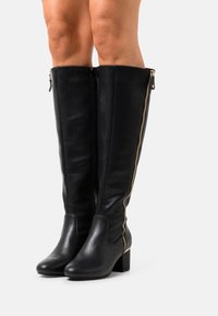 Botas negras de cuero hasta la rodilla con tacón grueso, con cremallera lateral y textura lisa, diseñadas para un ajuste ceñido.