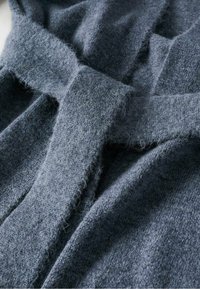 Szara dzianina o miękkiej, puszystej fakturze. Posiada szeroki pasek i nakładające się warstwy, prezentując przytulny, luźny fason.