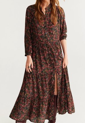 Lang blomsterkjole med mørkerøde, grønne og brune toner, med knapper og slid på siden, båret med brune knæhøje støvler.