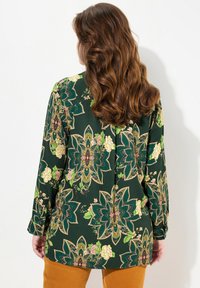 Green patterned blouse featuring floral designs, long sleeves, and a relaxed fit. Made of soft fabric with a smooth texture.