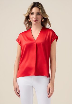 Blusa de satén roja con escote en V y mangas cortas enrolladas. Presenta un corte holgado y aberturas en los costados del dobladillo para facilitar el movimiento.