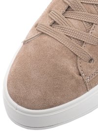 Close-up of beige suede sneaker with textured laces and white rubber sole visible at the bottom.