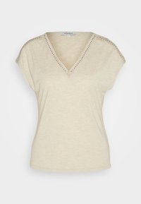 Haut beige à manches courtes et col en V avec bordure cloutée le long de l'encolure et des épaules, fabriqué en tissu léger, taille petite.