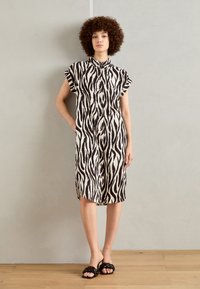 Fekete-fehér zebra mintás ingruha, rövid ujjú, gombos elülső rész, térd fölé érő hosszúság, könnyű anyag, fekete magassarkú szandálokkal viselve.
