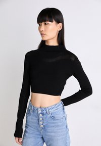Svart kortärmad topp med ribbad textur och subtila nätdetaljer, i kombination med ljusblå högmidjade jeans med knappar.