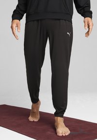 Pantalons de jogging noirs en tissu léger. Dotés d'une taille élastique et de poignets côtelés, avec un petit logo blanc sur le côté.