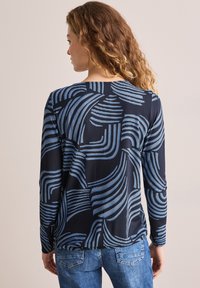 Haut à longues manches en bleu marine avec des motifs abstraits ondulés bleus, affichant une coupe décontractée et un tissu texturé. La vue arrière montre un ourlet arrondi.