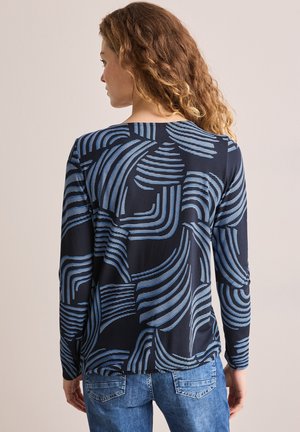 Haut à longues manches en bleu marine avec des motifs abstraits ondulés bleus, affichant une coupe décontractée et un tissu texturé. La vue arrière montre un ourlet arrondi.
