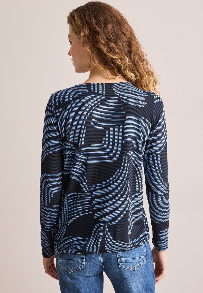 Haut à longues manches en bleu marine avec des motifs abstraits ondulés bleus, affichant une coupe décontractée et un tissu texturé. La vue arrière montre un ourlet arrondi.