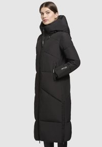 Manteau long noir rembourré avec un col haut, présentant des sections matelassées en diagonale, des poches latérales et une fermeture à glissière intégrale. Matériau imperméable.