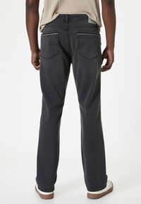 Jeans de mezclilla negra con un diseño de pierna recta, cinco bolsillos y detalles de costura sutiles, combinados con zapatillas blancas.