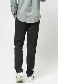 Mörkgrå sweatpants med avslappnad passform, elastisk midja och sidofickor, ihop med vita sneakers med blå detaljer.