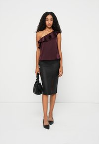 Burgundy satin topp med volangdesign på ena axeln, matchat med en figurnära svart läderkjol med en slits framtill, och en svart handväska.