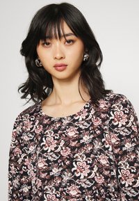 Blusa floral com fundo preto decorado com padrões de flores rosas e brancas, com decote redondo e textura de tecido leve.