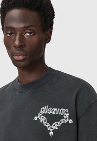 Hall peasärk, millel on ümmargune kaelus, esiküljel valgest ketist tehtud graafika ja rasvase fondiga "allsaints" tekst.