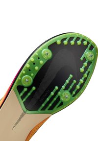 Semelle d'un crampon de football présentant une surface noire avec des crampons verts, un motif texturé et un accent beige près du bord.