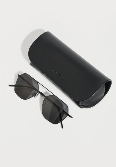 Γυαλιά ηλίου με μαύρο μεταλλικό σκελετό και σκούρους φακούς τοποθετημένα δίπλα σε μια μαύρη θήκη γυαλιών ηλίου με το λογότυπο Giorgio Armani πάνω σε λευκή επιφάνεια.