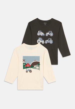 Deux chemises pour enfants à manches longues, une noire avec quatre illustrations de tracteurs, une crème avec une scène de ferme comprenant une grange, des animaux et un tracteur.