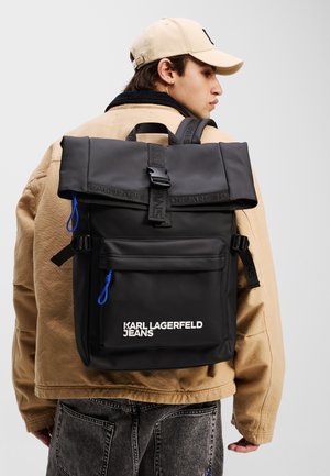 Black roll-top backpack with adjustable straps, blue zipper accents, and front pocket. Features logo text on the lower front panel.