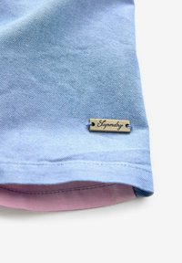 Lichtblauwe katoenen stof met een gestructureerd oppervlak. Voorzien van een messing label met "Superdry" graveerwerk en een roze accent op de interieurzoom.