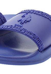 Purple rubber slide sandal featuring embossed logo and textured straps, with a flat sole and a slight sheen on the material.