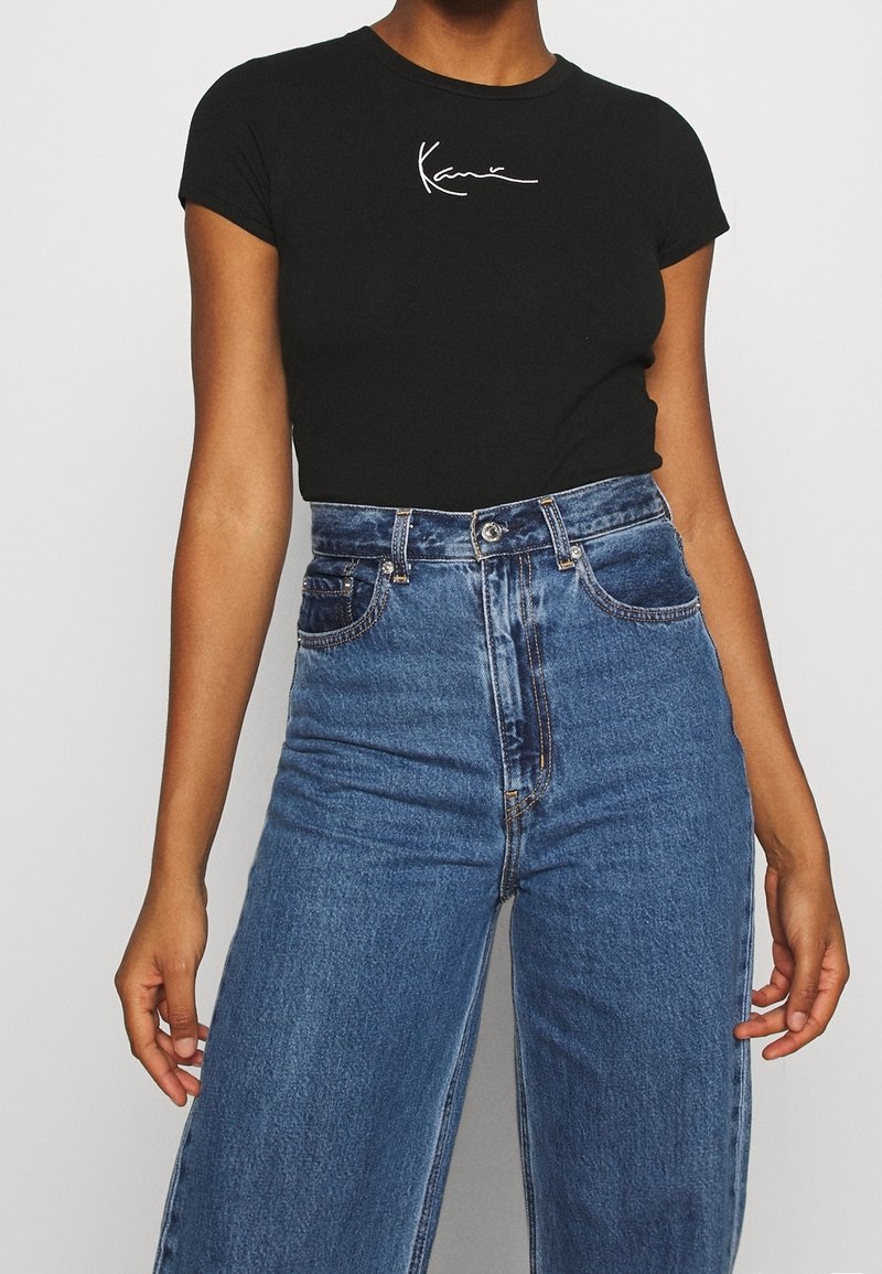 Černé přiléhavé tričko s krátkými rukávy, se vzorem bílého ručně psaného loga. Kombinováno s vysokými světle modrými džínovými kalhotami s širokými nohavicemi.