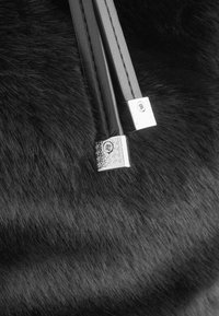 Gros plan sur un sac en fourrure noire avec des anses en cuir lisse et brillant, accentuées par des garnitures métalliques carrées et des surfaces texturées.