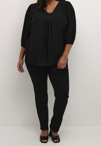 Completo d'abbigliamento nero composto da una blusa corta a maniche corte, con scollatura a V e parte frontale plissè, abbinata a pantaloni aderenti neri e scarpe open-toe.