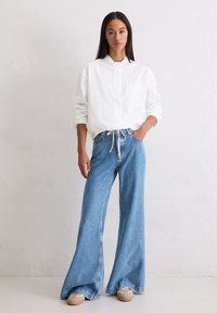 White button-up shirt with a collar, paired with light blue wide-leg jeans. Shoes feature a beige and gray color scheme.