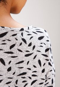 Pull gris avec des motifs noirs en forme de feuilles, présentant un col rond et une texture douce. L'accent est mis sur le détail du dos du tissu.