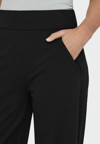 Czarne dopasowane spodnie wykonane z gładkiego materiału, z płaskim paskiem w talii i boczną kieszenią. Szwy nadają im uporządkowany wygląd.