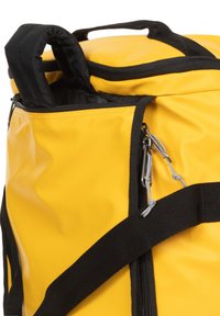 Bolsa de deporte impermeable amarilla con acentos negros, que incluye un bolsillo con cremallera, asas de transporte y correas ajustables para mayor comodidad.