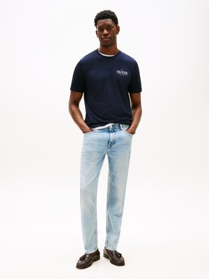 T-shirt de manga curta azul-marinho com logótipo branco, jeans de tom claro e sapatos pretos. Design simples, ajuste descontraído e textura de tecido suave.