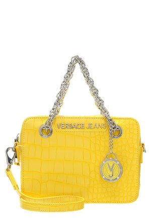 Gul taske med krokodilletekstur, sølvkædehåndtag, "VERSACE JEANS"-logo og rund mærkesmykke, der hænger fra det ene håndtag.