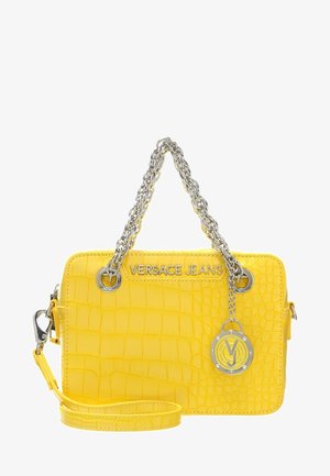 Borsa gialla con texture a coccodrillo, manici a catena argentata, logo "VERSACE JEANS" e ciondolo rotondo con marchio pendente da un manico.