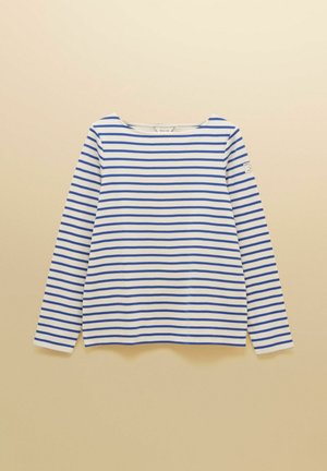 Weißes Langarmshirt mit gleichmäßig verteilten horizontalen blauen Streifen und einem kleinen Aufnäher am oberen linken Ärmel vor einem beigen Hintergrund.