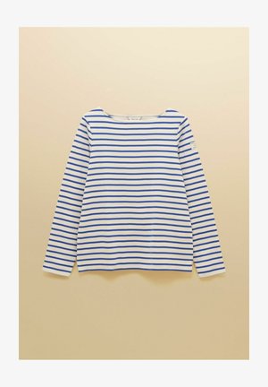 Chemise blanche à manches longues avec des rayures horizontales bleues uniformément espacées et un petit écusson sur la partie supérieure de la manche gauche sur un fond beige.